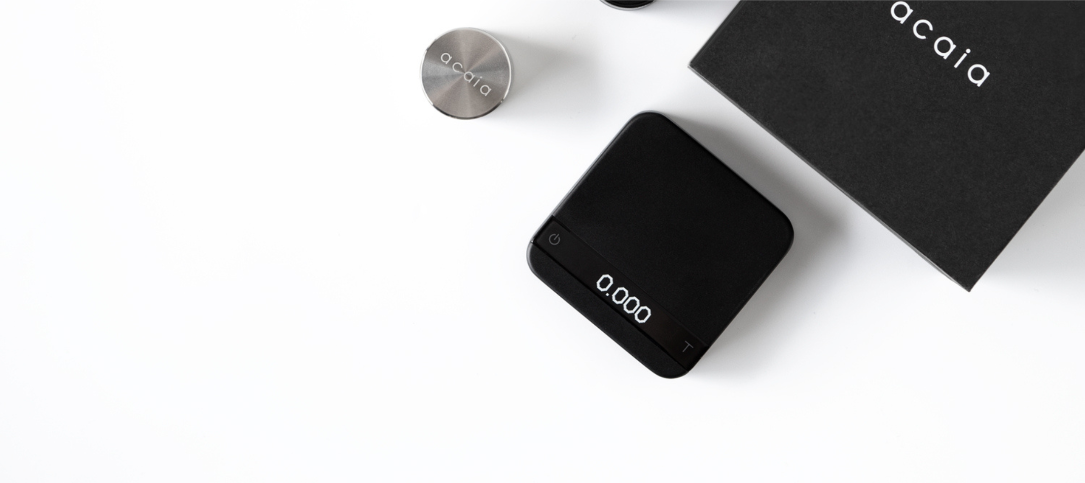 An above shot of the Pyxis Black, with a 100 gram calibration weight beside it and the packaging box above it.