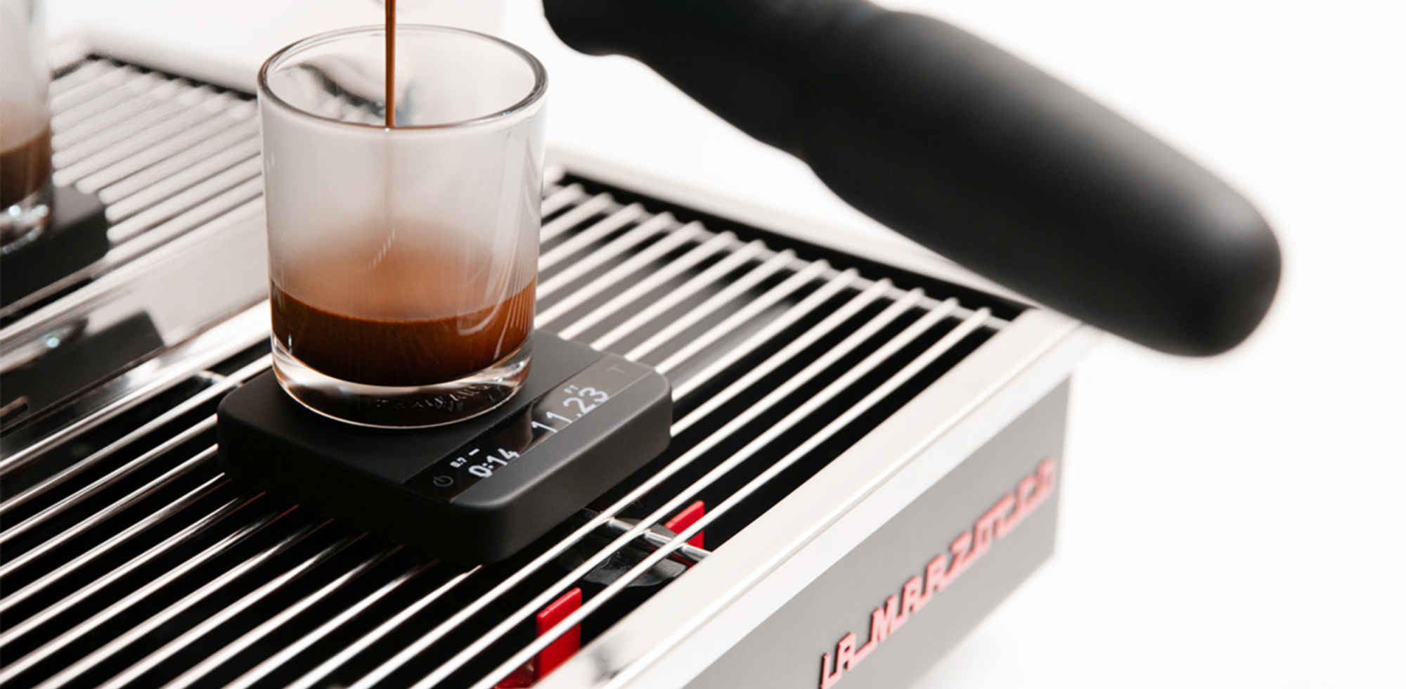 A Pyxis Black on a drip tray, seen from the side, with a glass espresso glass catching espresso